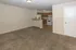 Spacious open-plan living area with cozy carpet leading to a modern kitchen featuring wooden cabinets and white appliances.