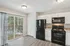Modern kitchen with sleek cabinetry, black appliances, and a bright sliding glass door leading to a wooden balcony with a charming view.