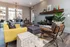 Inviting living room with modern decor, featuring a cozy fireplace, vibrant yellow sofa, stylish leather chairs, and natural light from large windows.