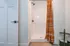 Modern bathroom featuring a sleek shower with an elegant orange stripe curtain, complemented by a stylish storage shelf and a contemporary door design.