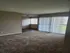 Bright living area with plush carpet and large windows offering plenty of natural light and a view of greenery.