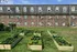Charming brick apartment building with vibrant raised garden beds and lush green lawn, perfect for nature lovers.