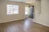 Inviting living room with sleek wood flooring, ample natural light from a large window, and contemporary entrance creating a welcoming atmosphere.