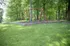 Peaceful playground with red swing set surrounded by lush greenery and mature trees, offering serene outdoor enjoyment.