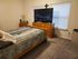 Inviting bedroom with a large TV, wooden dresser, and plush carpet.