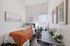 Cozy bedroom with modern decor, featuring a comfy bed with orange accents, sleek workspace, and vibrant indoor plants.