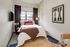 Cozy bedroom with a stylish decor, featuring a plush bed, modern artwork, and a soft rug for added comfort.