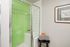 Modern bathroom with sleek glass shower featuring vibrant green tiles, complemented by a stylish wall art and cozy towels on a chic stool.