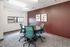 Modern meeting room with stylish teal chairs around a round table, vibrant maroon accent wall, and natural light from large window.
