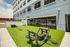 Modern outdoor fitness area with lush green turf and versatile workout equipment, adjacent to a residential building with a refreshing swimming pool view.