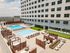 Luxurious apartment complex featuring a sunny rooftop terrace with multiple pools, lounging areas, and stylish fire pits.