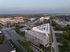 Cinematic aerial view of a modern apartment complex with ample parking, surrounded by lush greenery and cityscape, perfect for urban living.