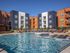 Modern apartment complex with vibrant orange and blue exteriors, featuring a large sparkling swimming pool and comfortable lounge chairs for relaxation.