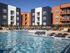 Modern apartment complex with vibrant exterior colors and a large, inviting swimming pool surrounded by stylish lounge chairs.