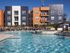 Contemporary apartment complex with vibrant orange and gray exteriors overlooking a sparkling swimming pool and sun deck.