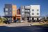 Modern apartment complex with colorful, geometric facade and ample parking under a clear blue sky.