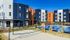 Modern apartment complex with vibrant colors, featuring a sparkling pool and a spacious sand volleyball court under a clear blue sky.