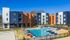 Vibrant apartment complex with modern architecture, featuring a spacious outdoor pool and sun lounging area under a clear blue sky.