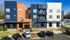 Modern apartment complex with vibrant blue and orange exterior, featuring balconies and adjacent parking, offering a stylish urban living environment.