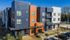 Contemporary apartment building with a vibrant facade featuring striking blue and orange sections, ample windows, and balconies, surrounded by lush landscaping and convenient parking.