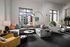 Modern apartment living room with stylish d&eacute;cor, featuring a cozy gray sectional sofa, colorful pillows, and large windows with city views.