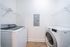 Modern laundry room with sleek washer and dryer, featuring wall-mounted shelving and bright lighting.