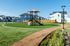 Modern community park with a playground, surrounded by suburban homes under a clear blue sky.