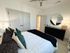Elegant bedroom featuring a plush bed with decorative pillows, sleek dark dresser with stylish decor, and a large round mirror enhancing the cozy ambiance.