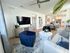 Modern living room with stylish blue armchair, elegant white sofa, and chic decor leading to an inviting dining area and contemporary kitchen.