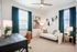 Bright and stylish home office with a comfortable sofa, elegant desk, modern decor, and large windows with green curtains.