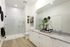 Elegant bathroom boasting a modern glass shower, sleek white cabinetry, and stylish decor with lush greenery.