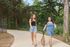 Two happy women walking a cute dog on a scenic nature trail, surrounded by lush trees and greenery.