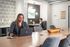 Modern co-working space featuring elegant table setup with a wooden centerpiece, stylish geometric wallpaper, and individuals working on laptops in a bright, contemporary environment.