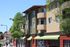 Charming modern apartment building with inviting balconies, surrounded by lush greenery and bright storefronts below.