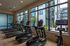 Modern fitness room with treadmills and exercise bikes, featuring large windows and a view of the stylish apartment complex exterior.