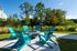 Inviting outdoor patio with vibrant turquoise chairs surrounding a modern fire pit, lush greenery and clear skies backdrop.