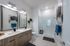 Elegant modern bathroom with dual sinks, stylish wood cabinetry, and a spacious glass-enclosed shower, complemented by chic lighting and decor.