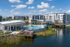 Luxurious lakeside apartment complex featuring a stunning pool, spacious sun deck, and modern architecture under a clear blue sky.