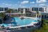 Luxurious apartment complex featuring a sparkling resort-style pool, modern lounge chairs, and vibrant umbrellas under a clear blue sky.