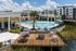 Luxurious apartment complex with a stunning resort-style pool area, stylish outdoor lounge spaces, and lush landscaping under a bright blue sky.