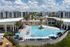 Luxurious apartment complex showcasing a stunning turquoise swimming pool surrounded by modern buildings and lush palm trees, offering a perfect blend of relaxation and contemporary living.