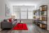 Modern living room with elegant grey sofa, vibrant red rug, and stylish shelving accents against a backdrop of large sunlit windows.