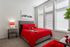 Bright and modern bedroom with red accents, cozy bed, and ample natural light from large windows.
