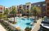 Luxurious apartment complex featuring a crystal-clear swimming pool, surrounded by stylish lounge chairs and palm trees, offering resort-style living.