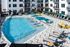 Luxurious apartment complex with a sparkling pool, chic loungers, and vibrant umbrellas, perfect for relaxation and leisure.