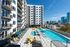 Modern high-rise apartment complex with spacious balconies overlooking a stylish rooftop pool and sun deck, set against a vibrant city skyline.