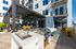 Modern outdoor entertainment space with stainless steel grill, shaded seating area, and sleek dining furniture in a contemporary apartment complex.
