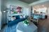 Modern open-concept living room with vibrant artwork, sleek furniture, and a stylish kitchen with bar seating.