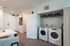 Modern apartment entry with chic laundry area, featuring front-loading washer and dryer, elegant white cabinetry, and sleek hardwood flooring.