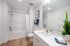 Modern bathroom featuring elegant wood flooring, sleek white vanity, and a cozy bathtub with chic tile design.